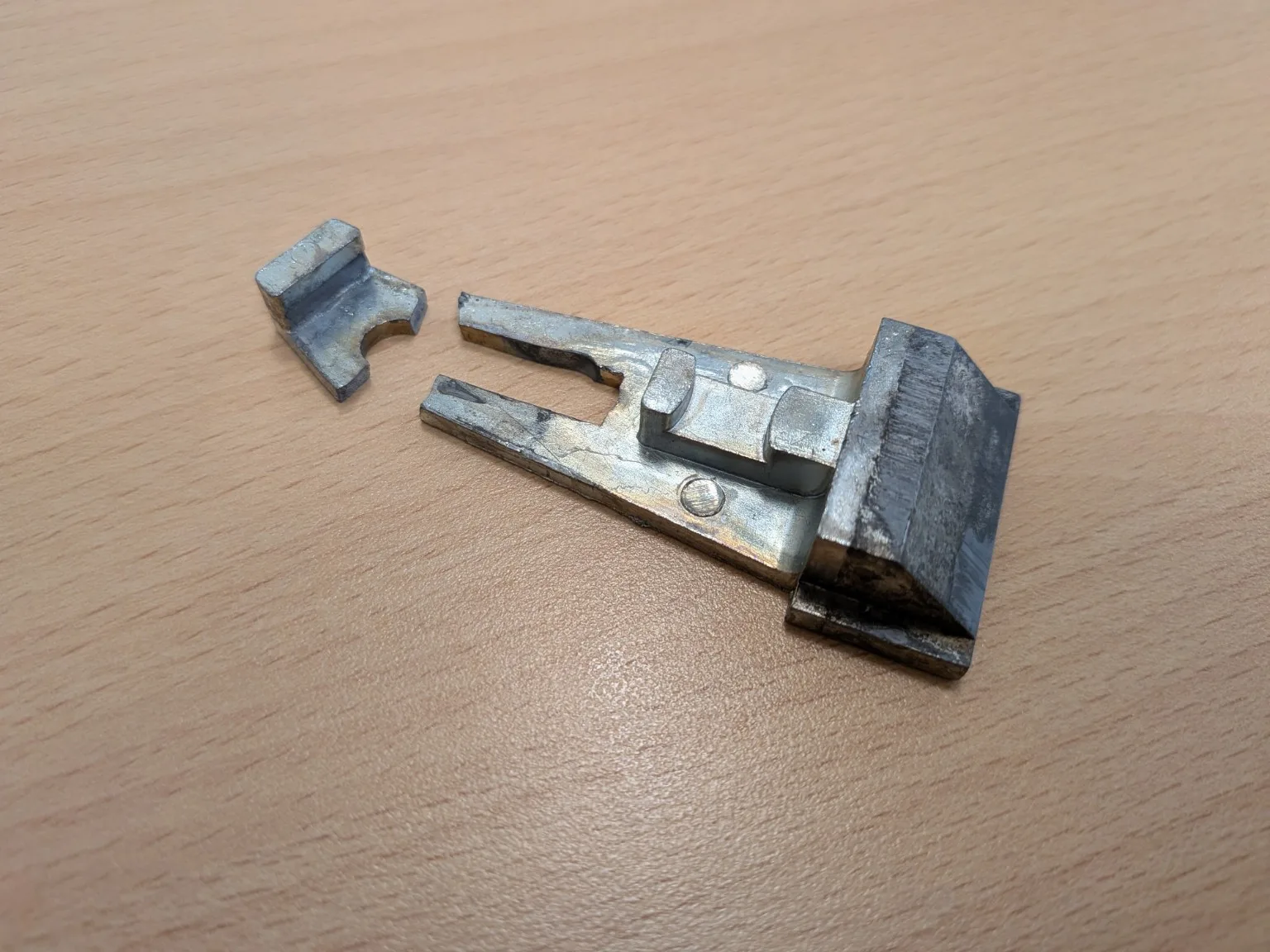Ausgebaute gebrochene Türfalle mit abgetrenntem Bruchstück auf einer Holzoberfläche.